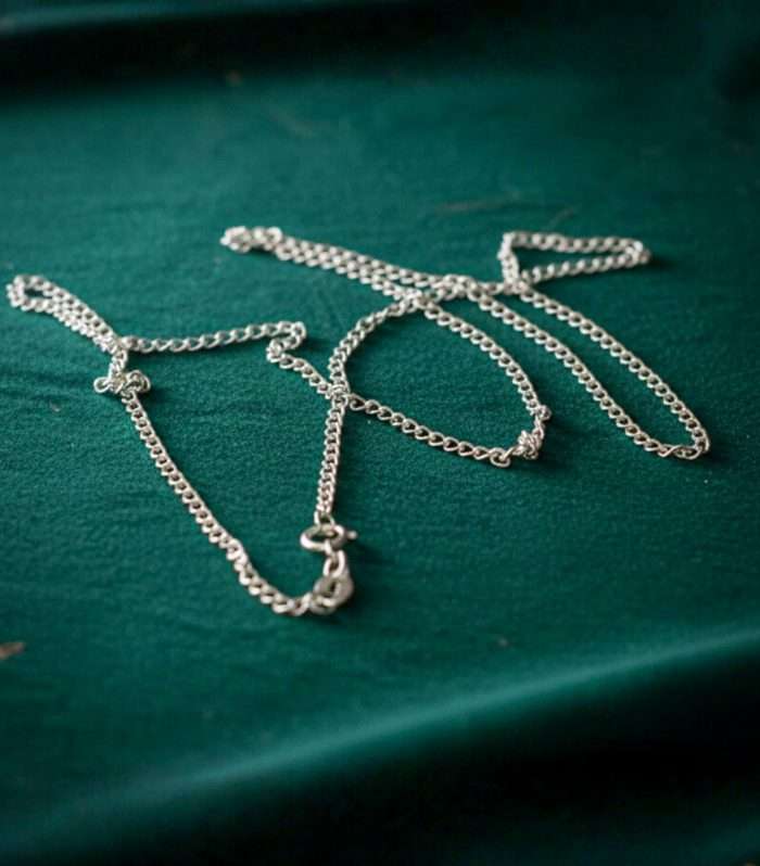 Collar largo de plata finamente pulida sobre superficie verde oscura, accesorio elegante para ocasiones especiales.